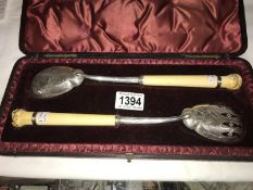A cased pair of silver and ivory salad servers with carved depiction of frog and fly.