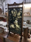 A wooden fire screen with a glazed embroidery of birds,