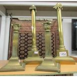 A pair of brass Corinthian column candlesticks and a pair of brass spring loaded candlesticks.