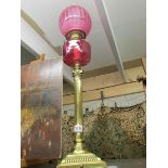 A brass oil lamp with cranberry glass font and shade.