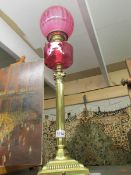 A brass oil lamp with cranberry glass font and shade.