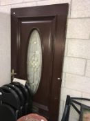 A heavy dark wood external door with oval glass insert