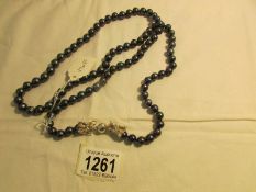 A black/navy pearl necklace with silver dragon fastening, 37" long.