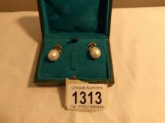 A pair of pearl drop earrings set with diamond bow tops in a green box.