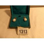 A pair of pearl drop earrings set with diamond bow tops in a green box.