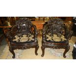 A pair of heavily carved Chinese chairs with tapestry cushions.