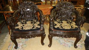 A pair of heavily carved Chinese chairs with tapestry cushions.