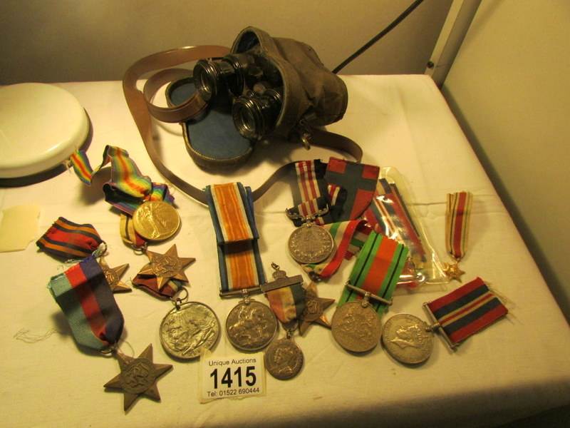 A quantity of medals with ribbons and a pair of military binoculars.