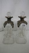 A pair of glass decanters with white metal collars and shoulders, one stopper a/f.