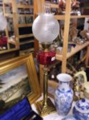 A brass Corinthian column oil lamp with cranberry glass font and later shade.