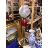 A brass Corinthian column oil lamp with cranberry glass font and later shade.