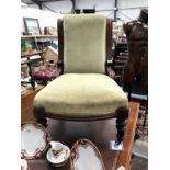 A carved wood frame nursing chair with green upholstery on casters