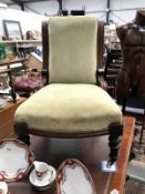 A carved wood frame nursing chair with green upholstery on casters