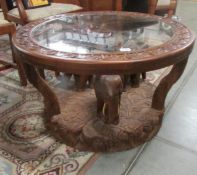 A carved coffee table with glass top having 3 elephants on base and elephants carved round rim.
