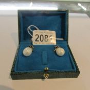A pair of pearl drop earrings set with diamonds bow tops in a green box.