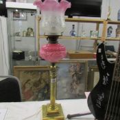 A brass Corinthian column oil lamp with pink glass font and later shade.