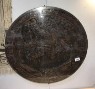 A large dark oak carved round wall hanging behind glass
