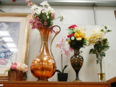 A large copper jug and gilded black metal vase with artificial flowers