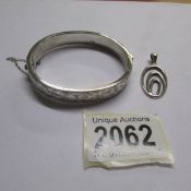 An engraved silver bangle with safety chain and a silver pendant.
