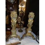 A pair of brass fire dogs as lion figures and a brass companion set.