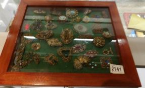 A glass case containing approximately 25 vintage brooches including some silver.