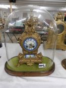 A gilt clock with enamel dial under glass dome.