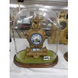 A gilt clock with enamel dial under glass dome.