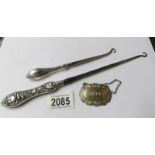 A large silver handled button hook, a smaller example and a silver wine label.