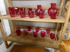 2 shelves of cranberry glass including jugs, bowls and wine glasses.