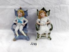A pair of bisque porcelain figures of boy and girl on chairs (boy a/f).
