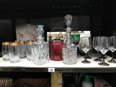 A shelf of drinking glasses, decanters, cranberry glass biscuit barrel etc.