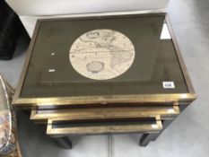 A nest of 3 tables featuring brass work and depictions of antique maps to top