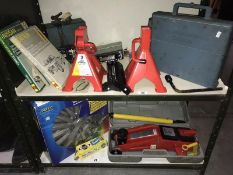 2 shelves of car related items including a cased jack, jack stands, battery chargers, hub caps etc.
