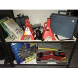 2 shelves of car related items including a cased jack, jack stands, battery chargers, hub caps etc.