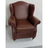 A wing backed armchair, upholstered in a brown leather, on turned and castor supports, 88cm w x 1m