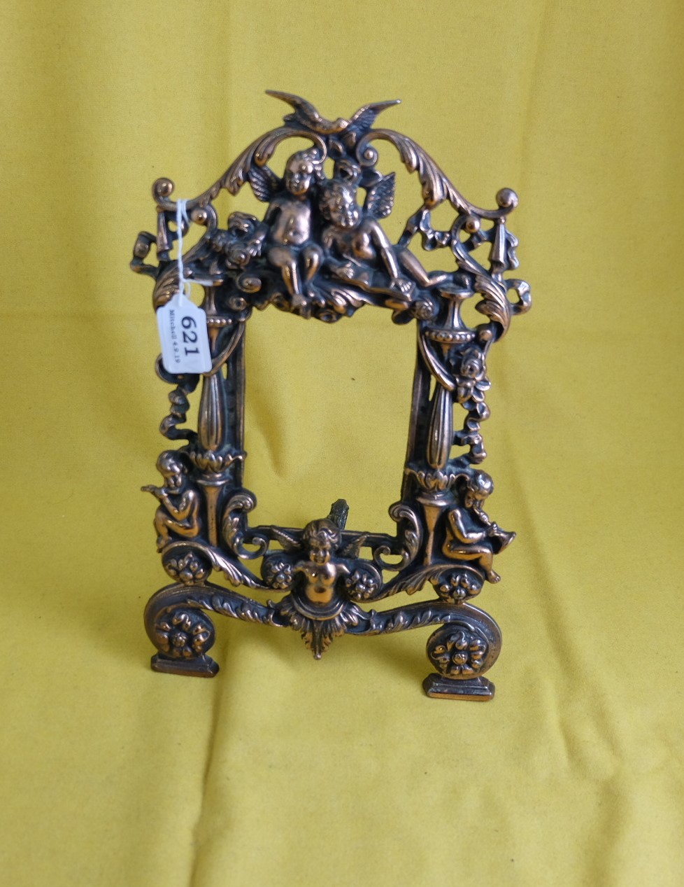 Copper toned photo frame on stand, registered number stamped on back, with musical cherubs and