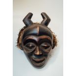 A Masquerade mask with filed teeth, round eye sockets, horns and bark cloth head piece.