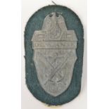 A Third Reich die cast zinc Demjansk arm shield, on field grey cloth with paper covered backing