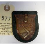A Third Reich Kuban arm shield, of bronzed zinc on field grey cloth patch with backing plate and