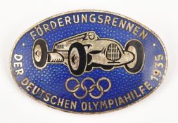 A Third Reich pin back oval enamelled badge, depicting a racing car (Mercedes?) above the Olympic