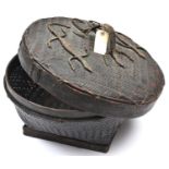 An African raffia woven circular casket, on squared base, the lid decorated with 3 lizards, the