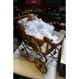 A Victorian style dolls pram. Steel framed with wickerwork body fitted with lace parasol, turned