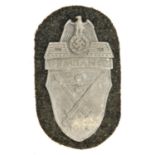 A Third Reich Demjansk shield, of zinc plated iron on field grey cloth patch with original paper