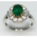 A contemporary Art Deco style emerald and diamond cluster ring, the oval cut emerald set within a