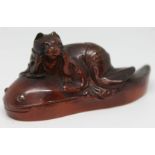 A Japanese carved amber coloured netsuke formed as a cat reclined upon a catfish, signature to base,