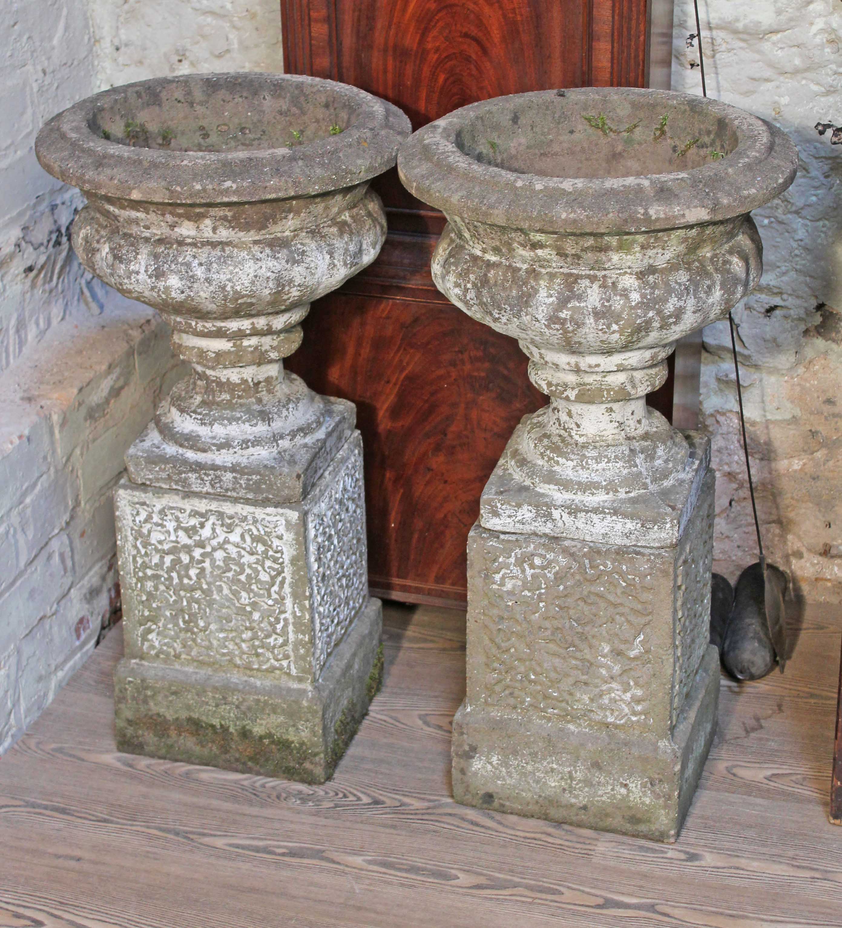 A pair of concrete garden urns on plinths, height 76cm.