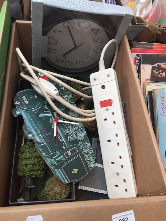 A box of items inc wall clock, gang plug, model railway items