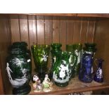 A shelf of Mary Gregory style green and some blue glass jugs and vases