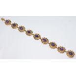 A contemporary gold and amethyst bracelet featuring nine flower head links each set with an amethyst
