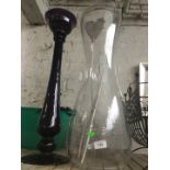 A large clear hourglass shaped vase and an amethyst coloured tall vase in shape of column.